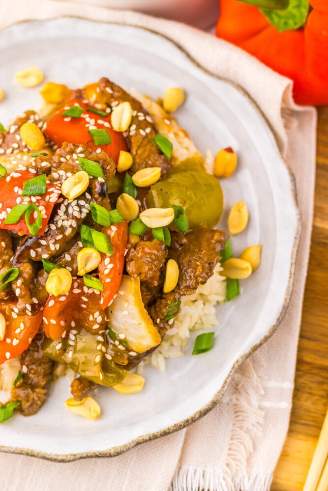 Vibrant beef and vegetable stir-fry with peanuts and sesame seeds on a white plate.