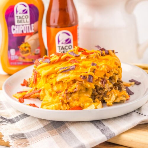 Delicious loaded taco casserole with chips, cheese, and toppings on a white plate.