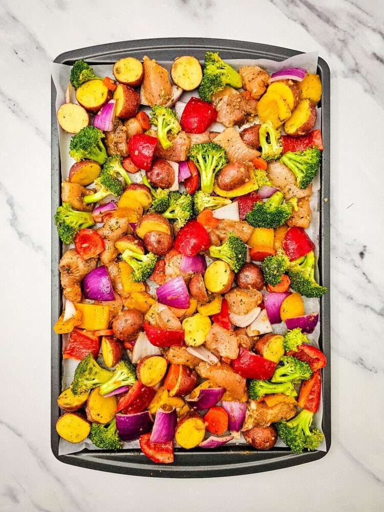 Sheet pan sriracha ranch chicken with roasted vegetables - golden browned chicken, yellow potatoes, green broccoli, and red bell peppers on parchment paper