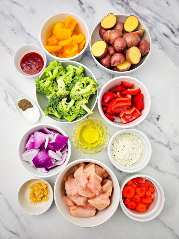 Assorted fresh vegetables, chicken, and seasonings for cooking.