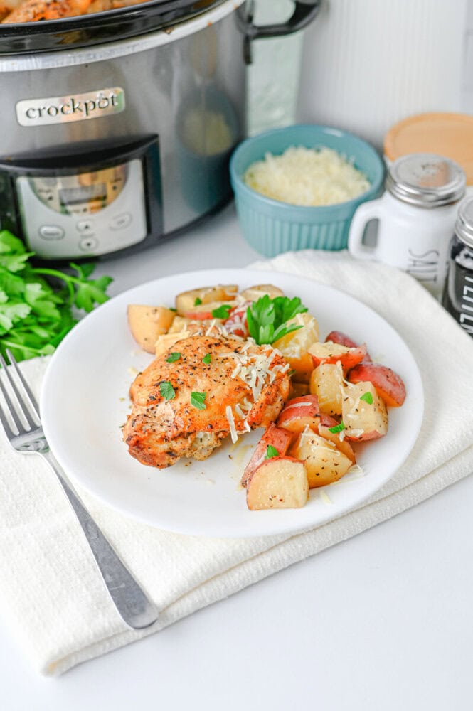 Slow cooker garlic parmesan chicken and potatoes plated on white dish with fresh parsley garnish and grated cheese