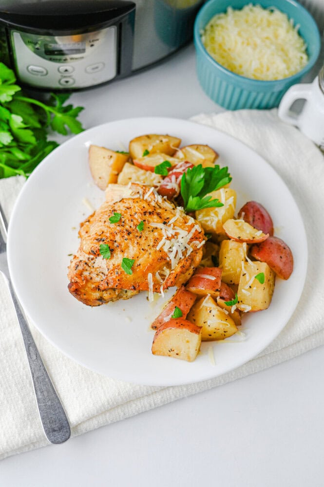 Slow cooker garlic parmesan chicken with roasted potatoes and sausage plated on white dish with fresh parsley garnish