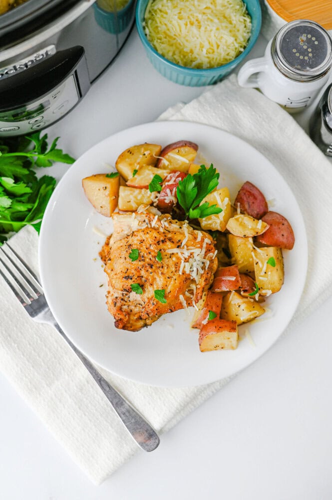 Crispy baked chicken served with roasted potatoes and fresh parsley on a white plate.