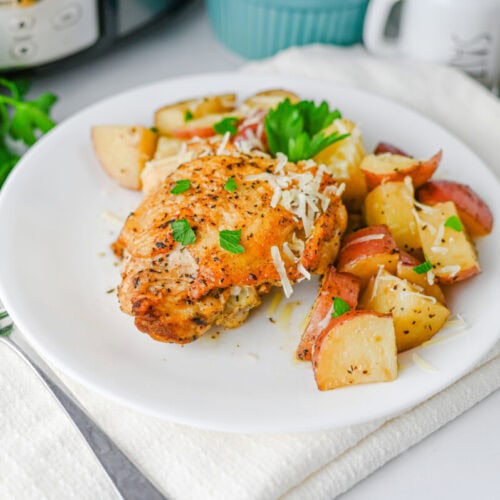 Baked chicken served with roasted potatoes and fresh herbs on a white plate.