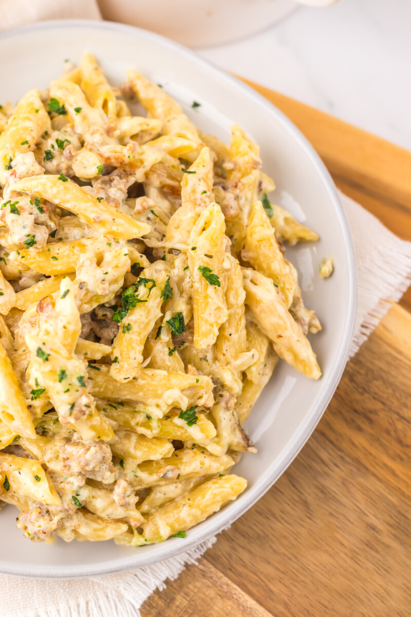 Creamy chicken pasta with herbs in a white bowl on a wooden surface.