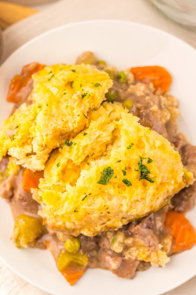 Golden chicken pot pie with flaky crust and mixed vegetables on a white plate.