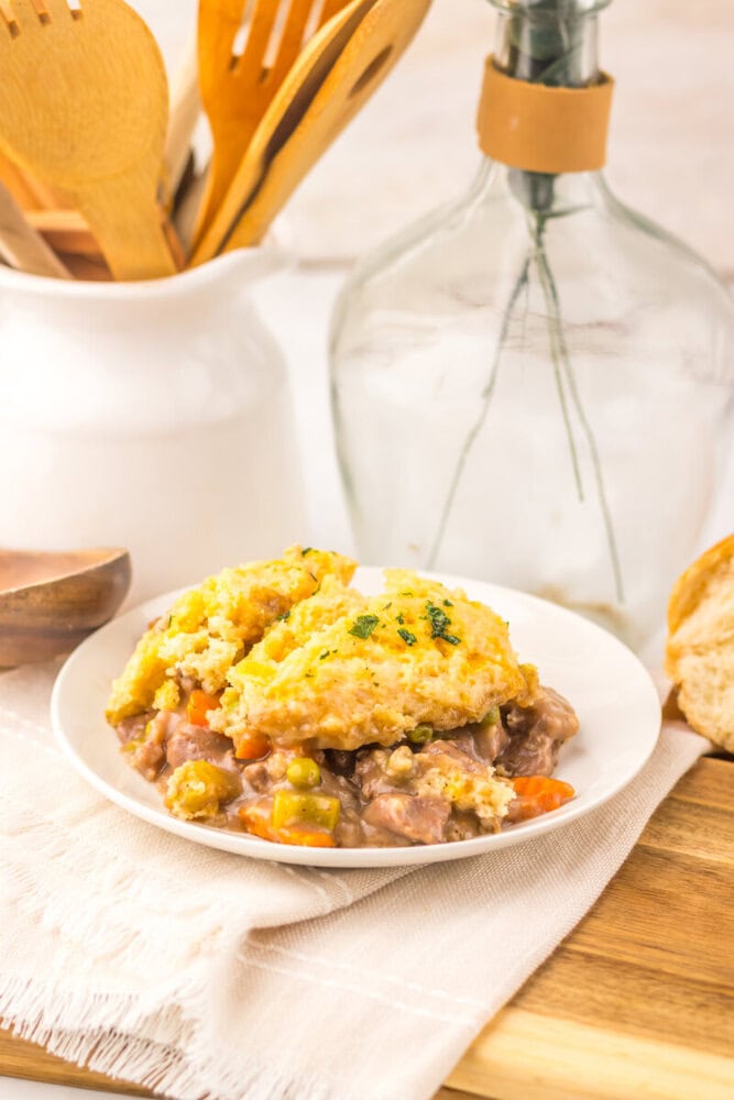 Slow cooker cheddar bay beef pot pie with golden biscuit topping and vegetable filling on white plate